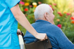 Rückansicht eines Seniors im Rollstuhl, der von einer Pflegekraft geschoben wird