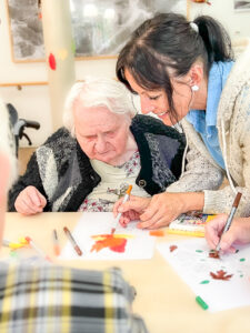 Eine Betreuungskraft hilft einer Seniorin beim Malen mit Filzstiften