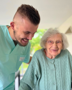 ein junger Pfleger mit lächelnd mit einer Seniorin